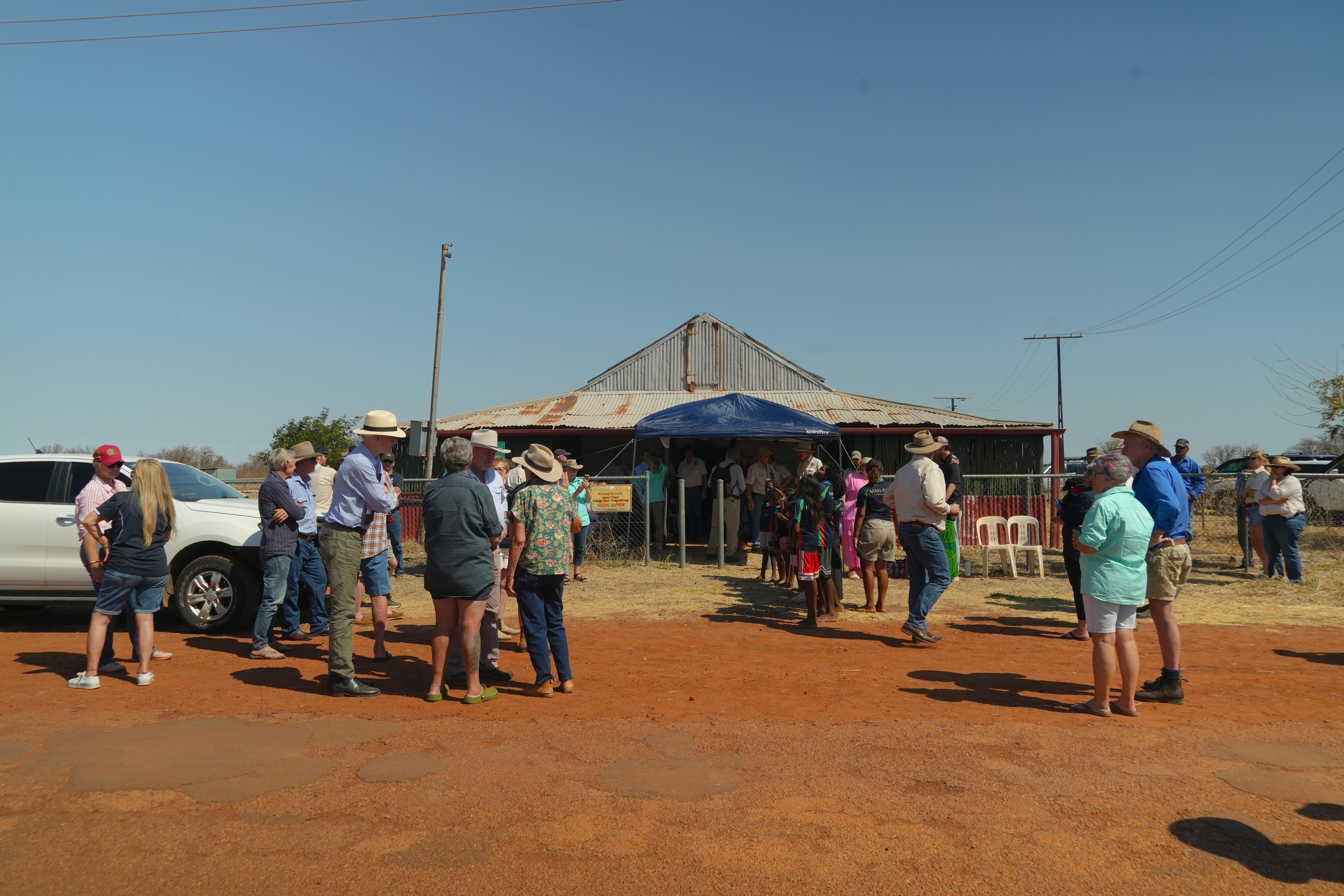 A group of people on a dirt road in front of an abandoned old building.