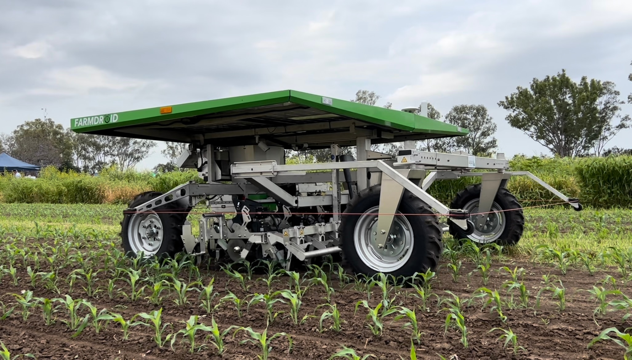 A green robot with solar panels on the top drives through a paddock.