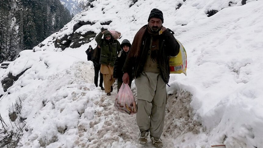 Kashmir villager walk through snow-covered road with bags in their hands.