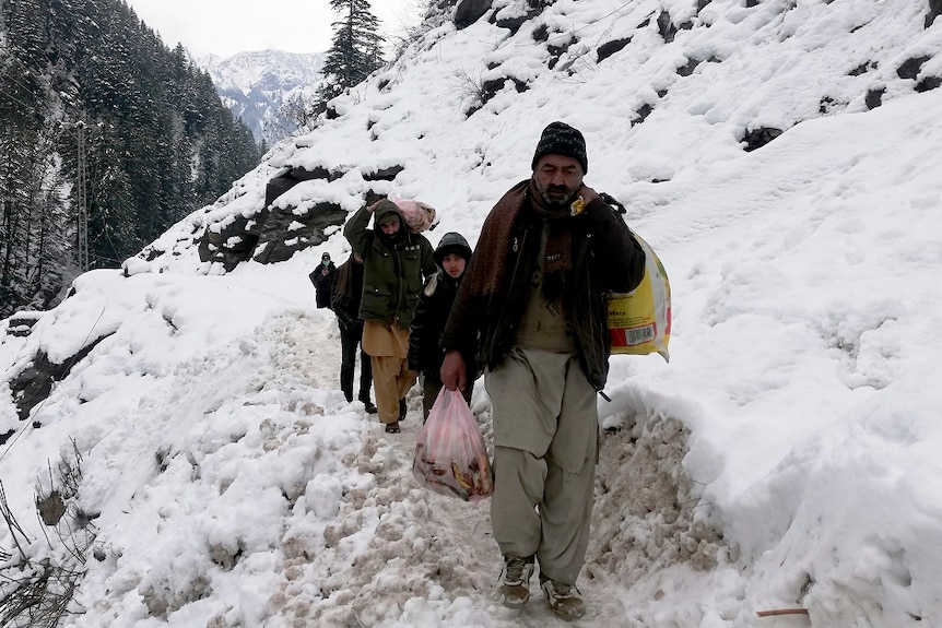 Kashmir villager walk through snow-covered road with bags in their hands.