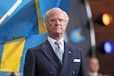 Sweden's King Carl XVI Gustaf stands in front of the national flag