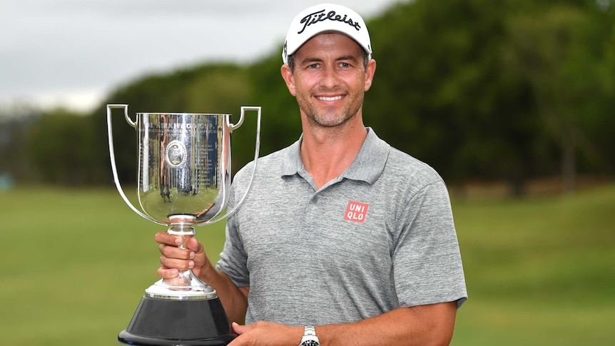 A smiling golfer holds a large trophy in his right hand, supporting it with his left.