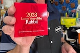 A man in a blue polo shirt holding a small red folder with 2023 Lunar Year of the Rabbit on the front.