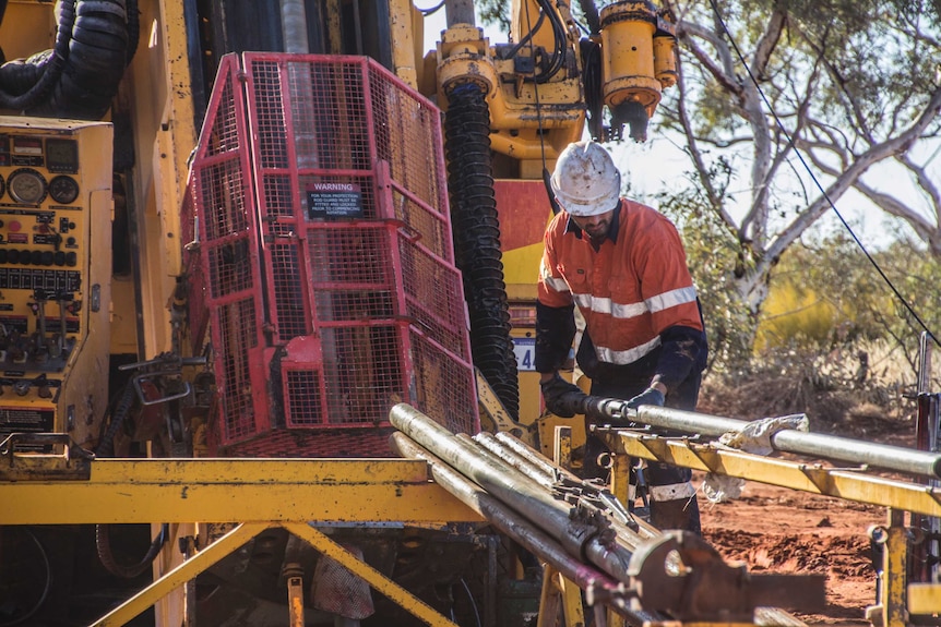 A mining worker wearing high-vis clothing in remote bushland working on a drill rig.