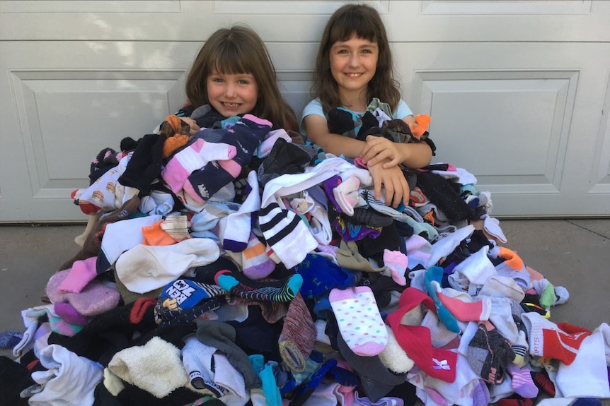 Two dark haired young girls sit in a large pile of socks.