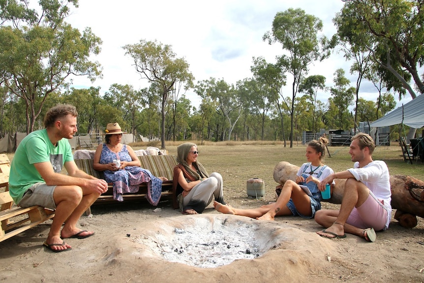 Casually-dressed people sitting around a campfire talking in a bush setting