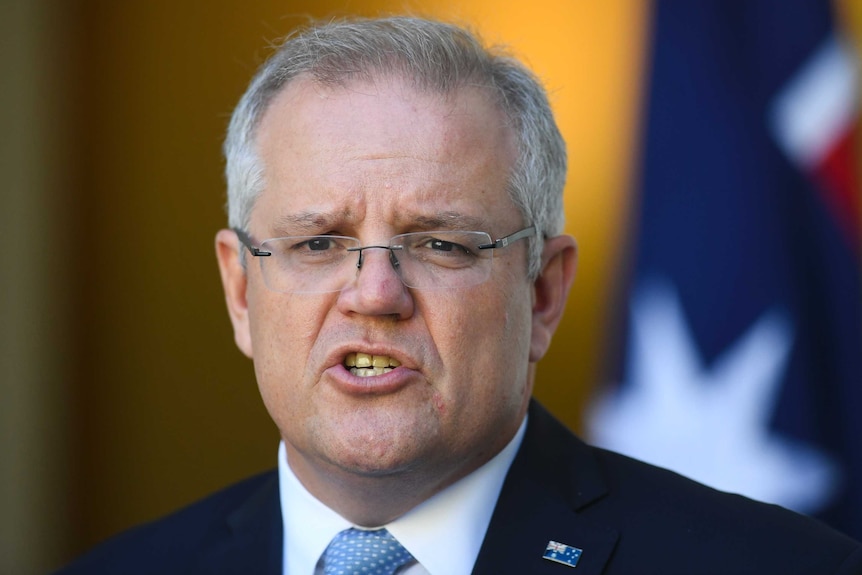 Scott Morrison purses his lips while speaking. An Australian flag is behind him.