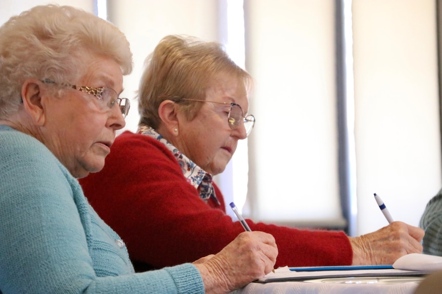 Two elderly woman write notes.