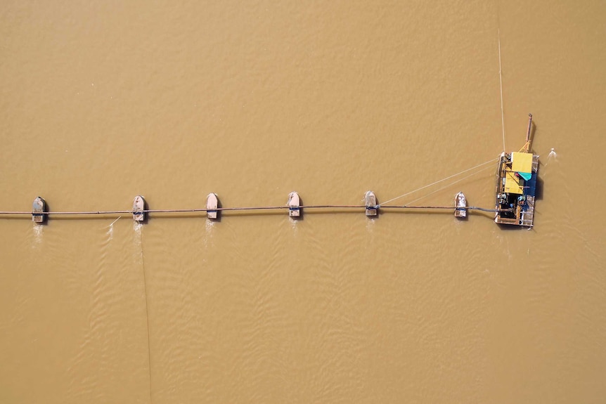 Aerial view of a large brown body of water, upon which sits a long pipe, with small machines connected to it at even intervals.