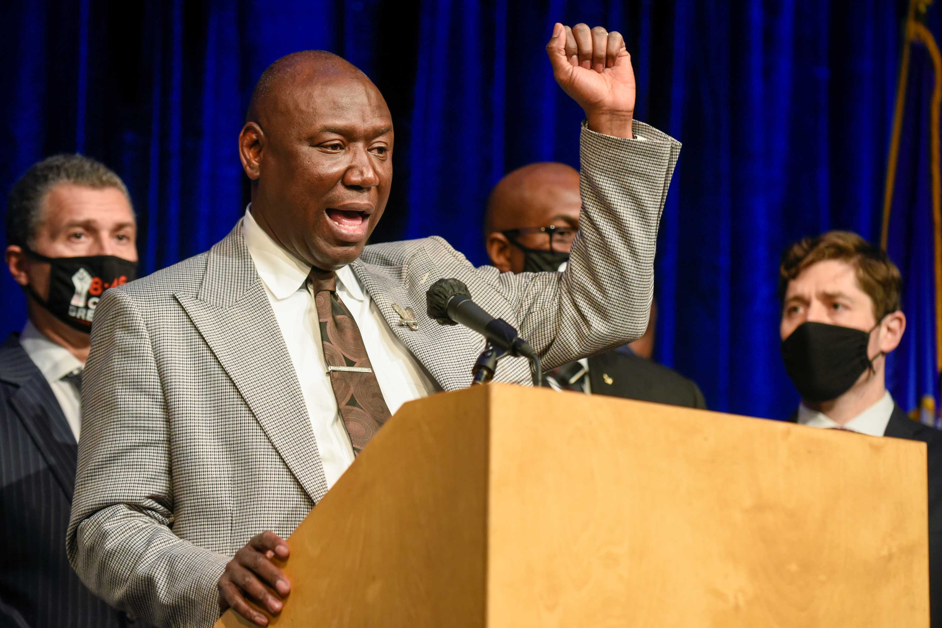 A middle-aged black man in a light suit raises his left arm in triumph in front of masked officials.