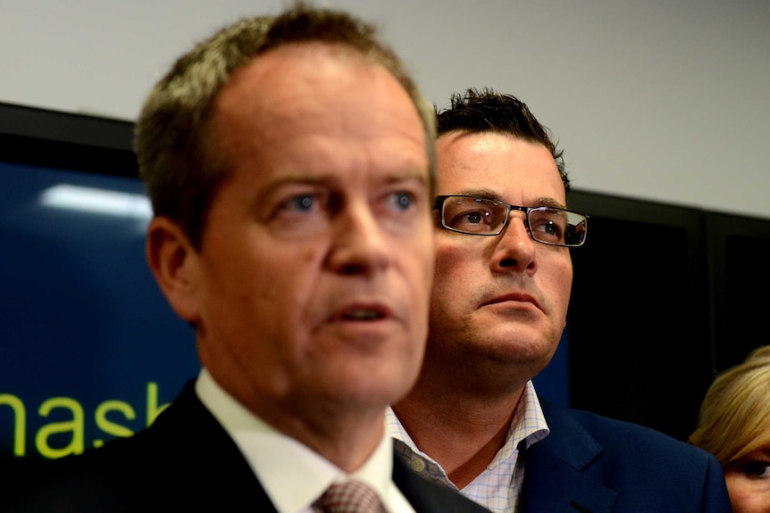 Bill Shorten speaks at a press conference as Daniel Andrews, who wears glasses, stands behind him.