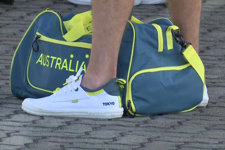 Legs of an athlete with sneakers labelled Tokyo with an Australia bag