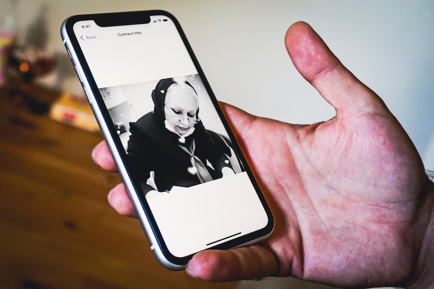 A hand holds an iPhone with a black and white photo of an elderly woman.