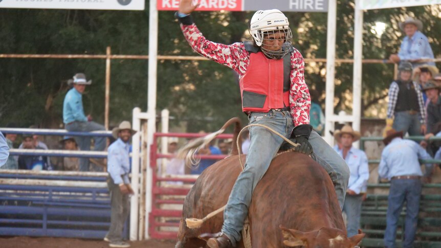 a woman rides a bull in a rodeo arena