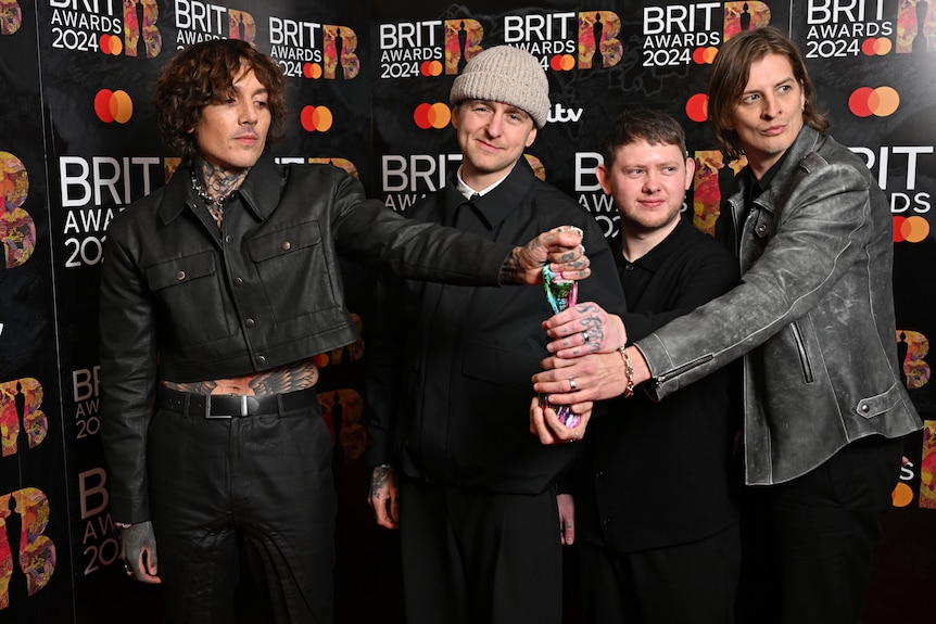 Four men in dark clothing all hold their BRIT