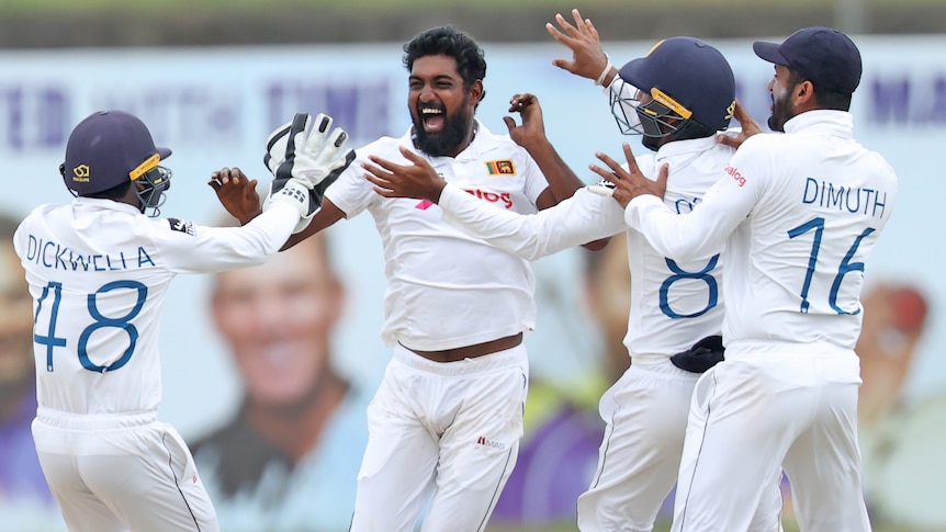 Prabath Jayasuriya smiles and holds his hands up as his teammates run to him to high-five him.