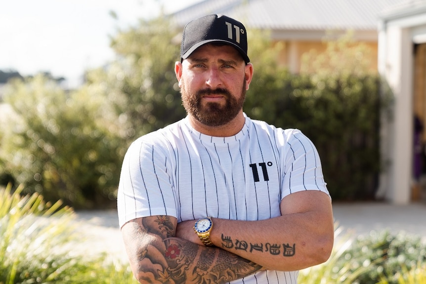 Man with folded arms in baseball cap stares at the camera