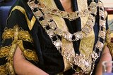 Gold chain and medallions worn on top of a black and gold brocade coat