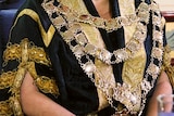 Gold chain and medallions worn on top of a black and gold brocade coat