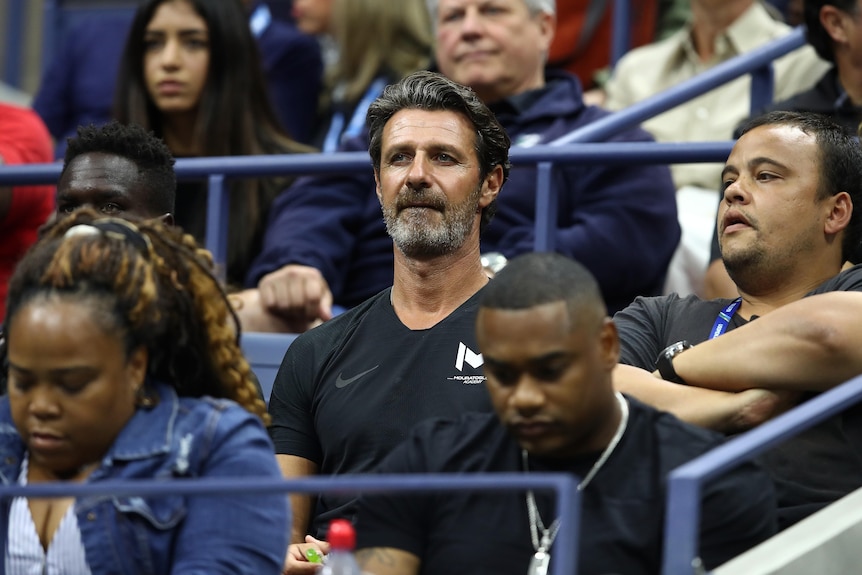 Tennis coach Patrick Mouratoglou sits in the grandstand at the US Open final, staring at the court. 