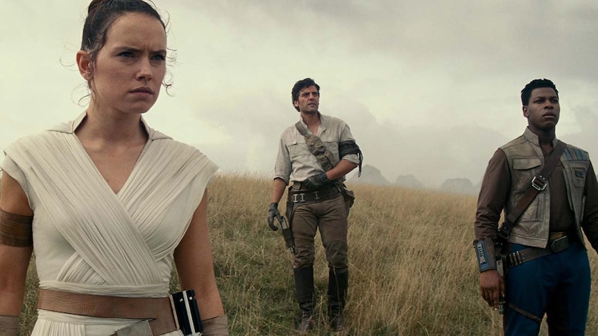 A scene from The Rise of Skywalker showing the characters of Rey, Poe, and Finn walking across grass looking serious.