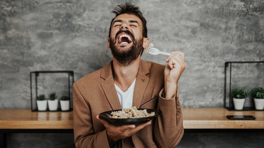 man in suit eating a bowl of pasta and laughing