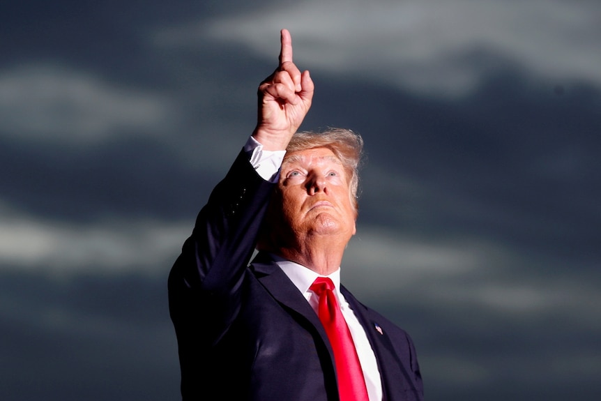 Donald Trump points to a stormy sky 