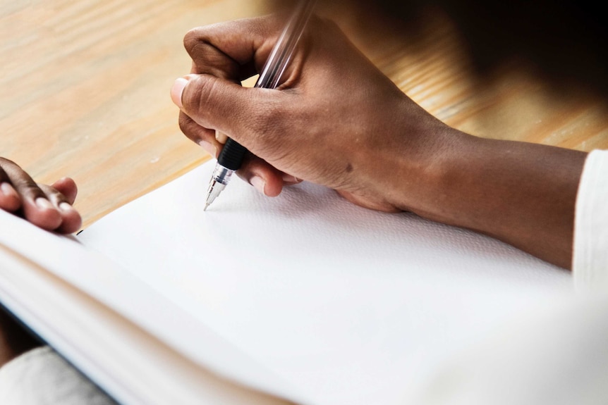 Close up of woman's hand as she writes in a blank notebook, depicting the need to keep notes of instances of workplace conflict.