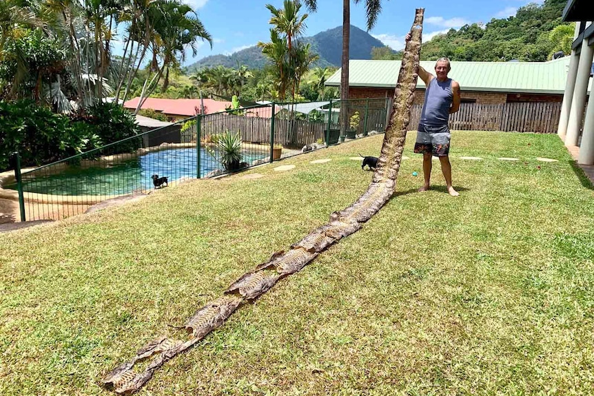 A man holding a very long snake skin in a Cairns backyard