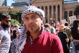 a man in a red polo shirt and a black and white keffiyeh looks directly into the camera with a serious expression