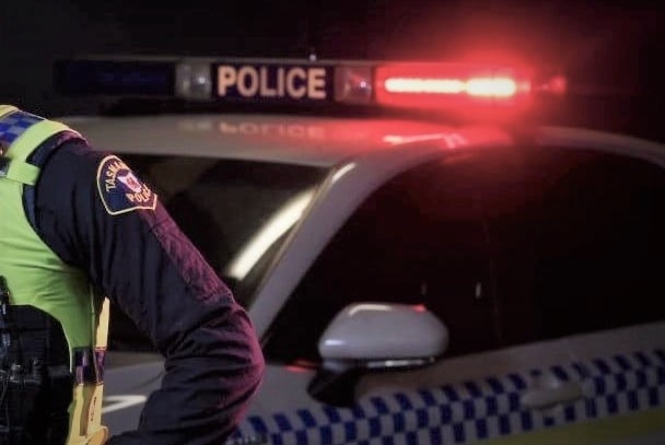 Flashing lights on Tasmania Police car with unidentified officer nearby.