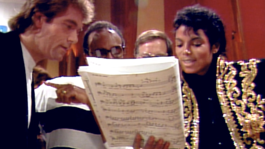 Michael Jackson and other musicians look over sheet music together in a music studio.