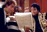 Michael Jackson and other musicians look over sheet music together in a music studio.