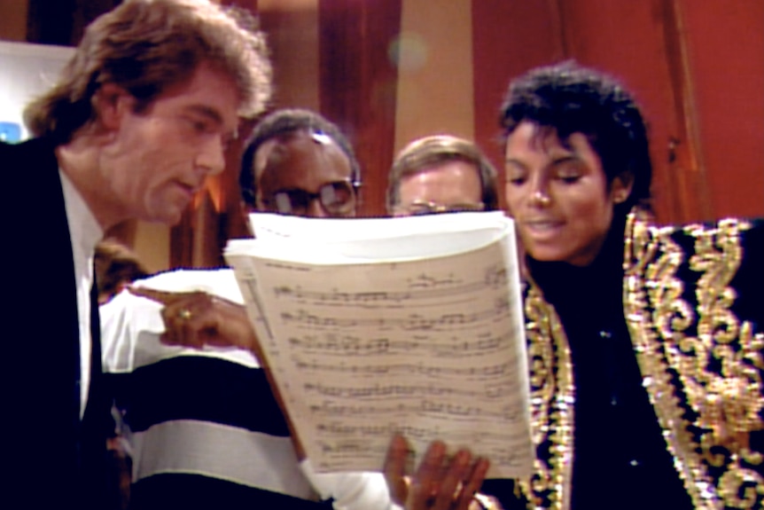 Michael Jackson and other musicians look over sheet music together in a music studio.