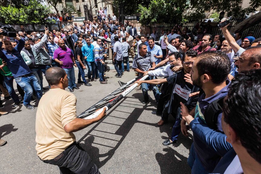 Egyptian journalists attempt to move a barricade into place on a street as dozens of people look on.