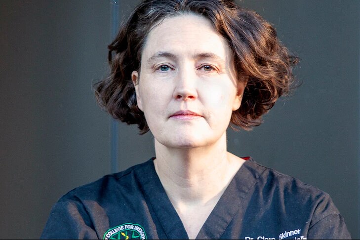 A woman wearing medical scrubs with a serious expression