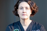 A woman wearing medical scrubs with a serious expression
