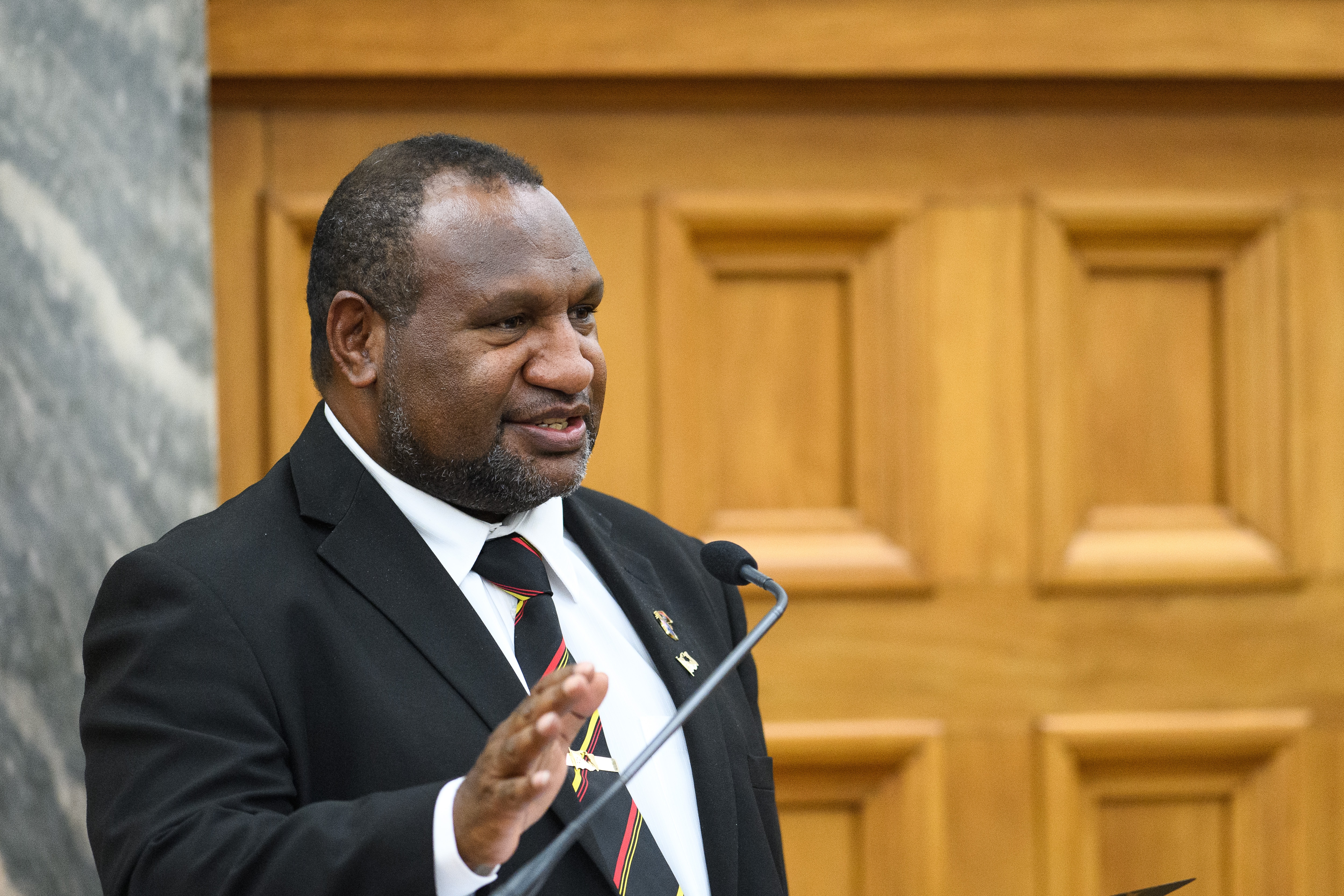 Mam in suit speaking on podium, with smile