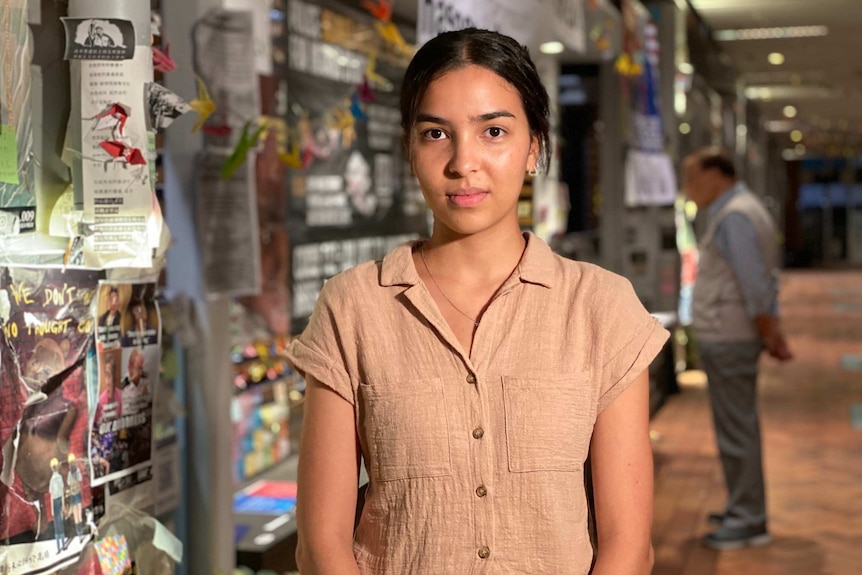 A woman stands in front of a wall plastered with posters and paper.