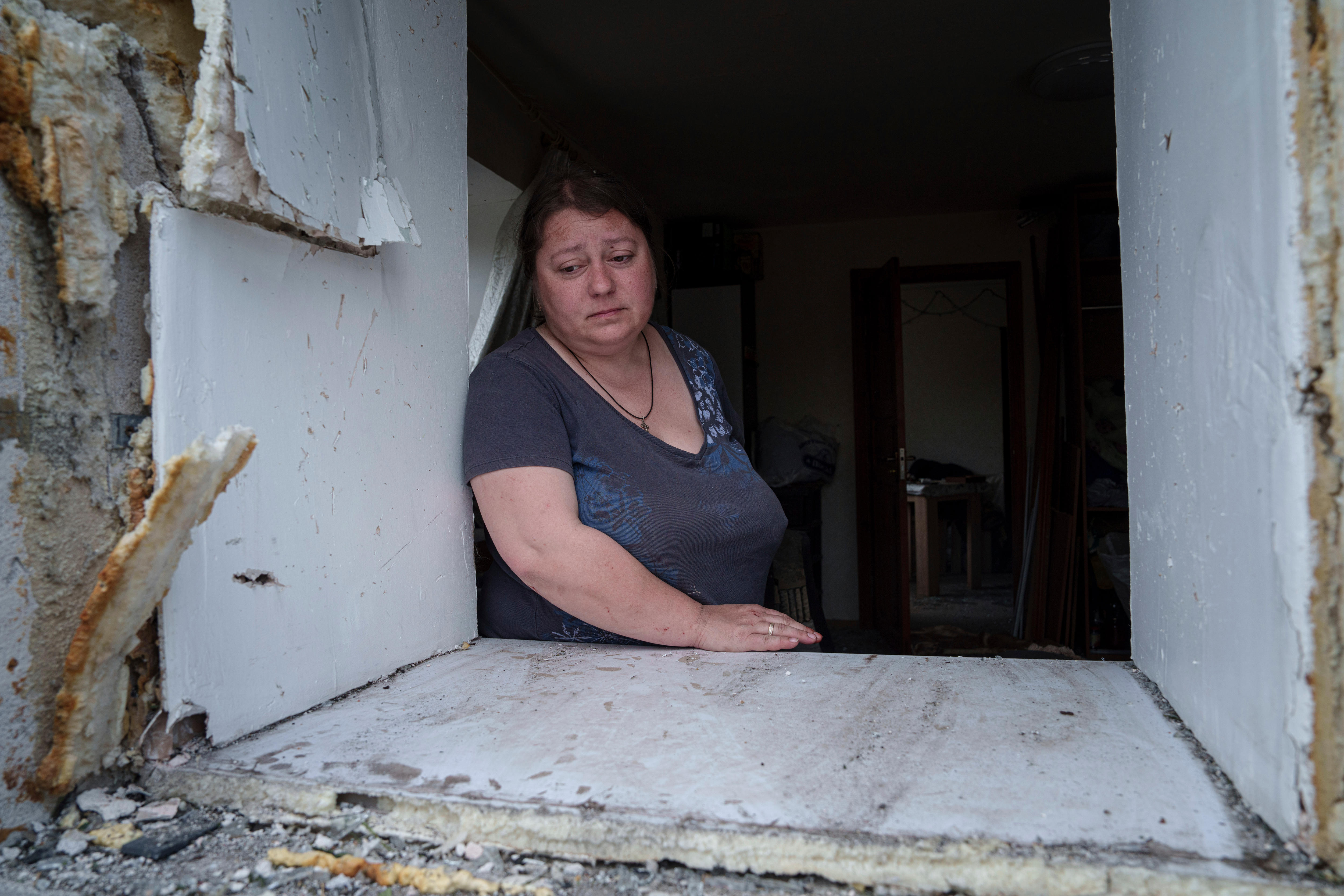 A women looks out a window damaged in strikes. 