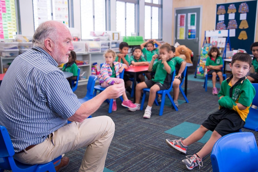 Dr John Munro sits with children in a classroom at Cairns West State School.
