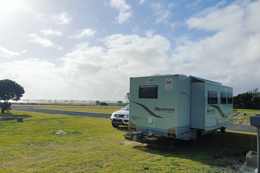 A grassy area with a parked car and caravan, the ocean in the background