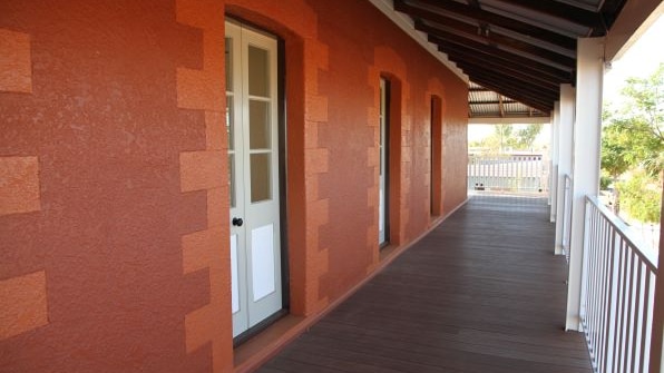 A wooden verandah with a white railing and a red wall.