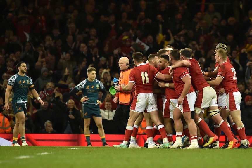 A group of Welsh rugby players hug and celebrate after the final whistle, as two Australian players watch on, dejected.