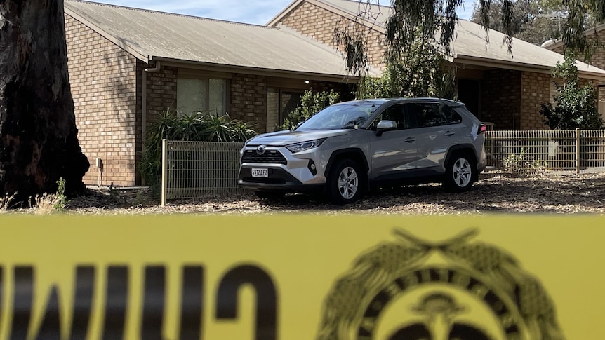 A car parked outside a home, with police tape in the foreground.