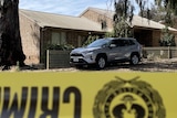 A car parked outside a home, with police tape in the foreground.
