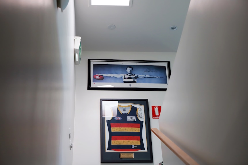 Escada levando a duas paredes emolduradas com uma bola de futebol americano e uma foto de Patrick Dangerfield