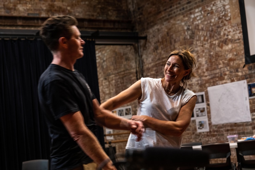Claudia Karvan grabs co-star Nathan Page's arm during rehearsals in a brick-walled room.