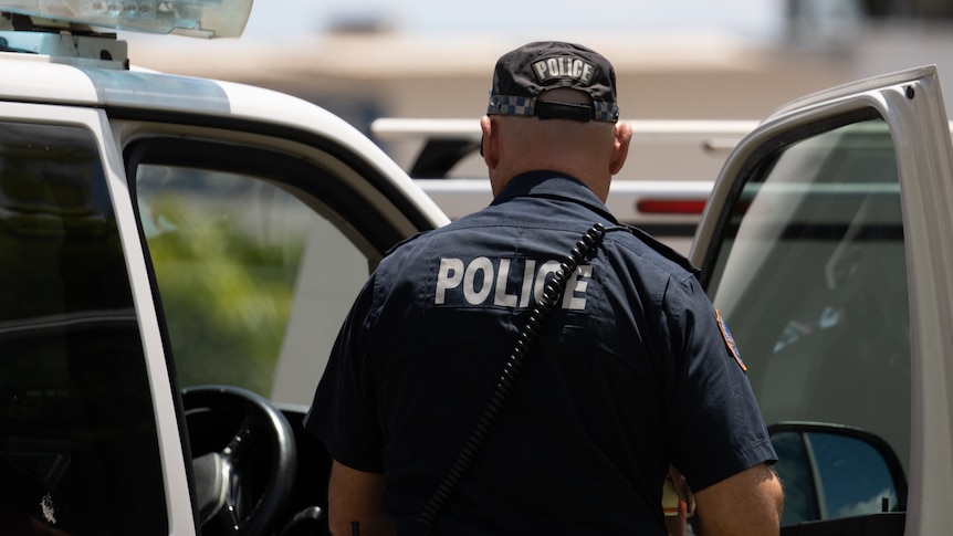 An NT police officer standing next to a police vehicle, with his back the camera, on a sunny day.