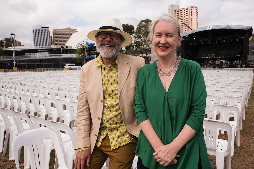 Neil and Rachel lean on chairs in front of a stage in Elder Park.